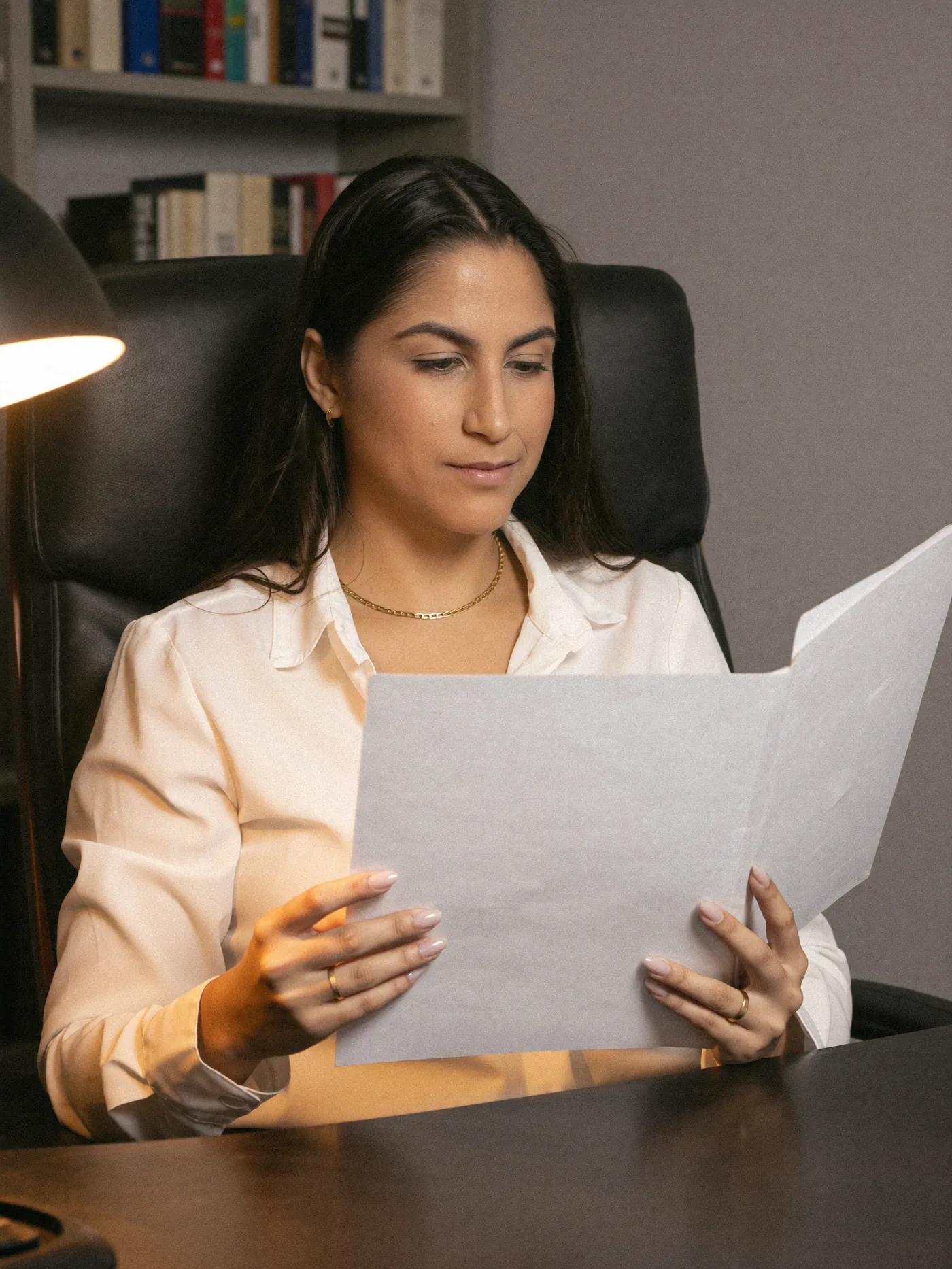 Jennifer Paim lendo um processo no escritório, à luz de um abajur